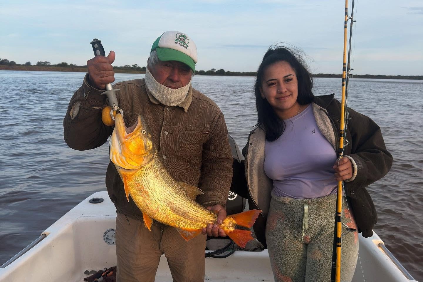 Pescador y pescadora con un dorado en la lancha durante una salida de pesca de día, Esquina, Corrientes
