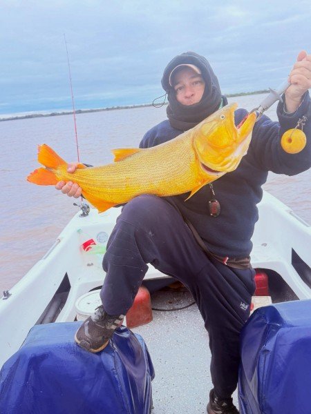 Pescador con capucha levanta un gran dorado en la lancha, Esquina, Corrientes