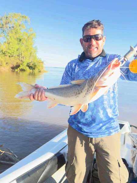 Pescador con anteojos de sol muestra su captura junto a la costa, Esquina, Corrientes