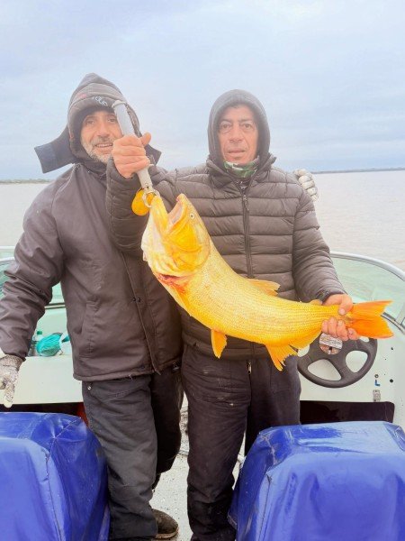 Dos pescadores abrigados sostienen un dorado en la lancha, Esquina, Corrientes