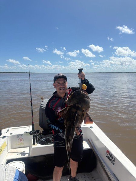 Pescador con un gran pez de cuero en la lancha bajo el cielo azul, Esquina, Corrientes