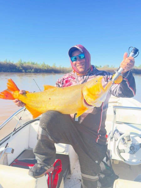 Pescador con anteojos espejados y un gran dorado, monte de la costa de fondo, Esquina, Corrientes