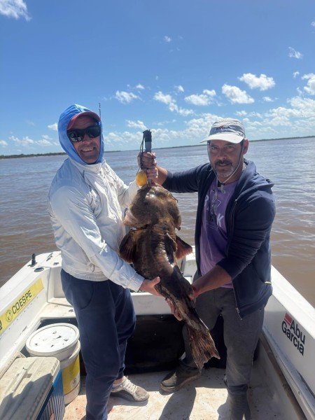 Dos pescadores sostienen un gran pez de cuero en la lancha, Esquina, Corrientes