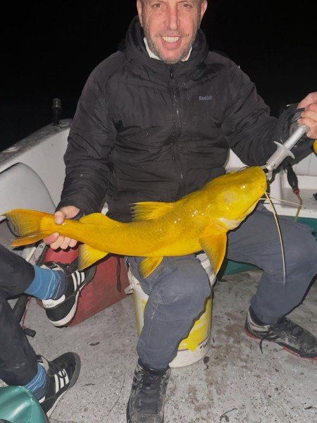 Pescador sentado muestra un pez de cuero amarillo de noche, Esquina, Corrientes