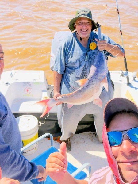 Pescador con sombrero muestra su captura y un amigo en primer plano, Esquina, Corrientes